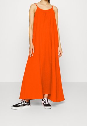 Oranje, mouwloze maxi-jurk met een geplooide halslijn. Gecombineerd met zwarte sneakers met witte zolen en roze veters.