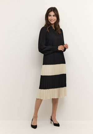 Abito plissettato nero e crema con maniche lunghe, scollo a V e una silhouette fluida con blocchi di colore alternati.