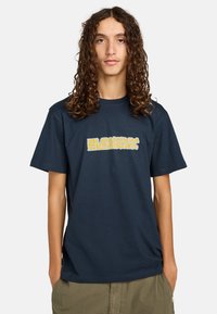 Mørkeblå bomulds T-shirt med et stiliseret gult grafisk design på forsiden. Korte ærmer og rund halsudskæring. Løs pasform.