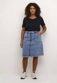Denim skirt with a mid-length cut, featuring two side pockets, a central zipper, and a belted waist, paired with a black short-sleeved top.