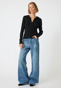 Svart ribbad zip-up hoodie med huva, tillsammans med vida blå denimjeans. Outfitten kompletteras av svarta skor och en avslappnad passform.