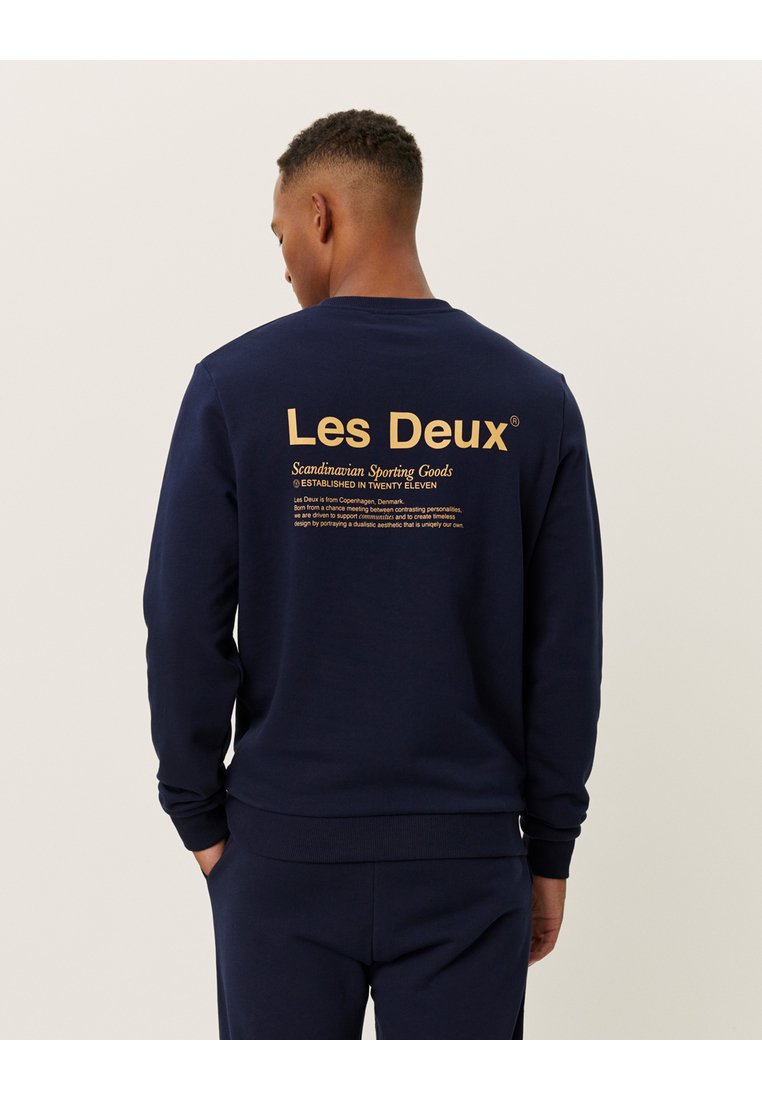 Navy blue sweatshirt featuring a round neckline, ribbed cuffs and hem, with gold text branding and details printed on the back.