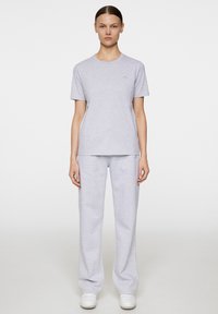 Szara bawełniana koszulka z krótkim rękawem i okrągłym dekoltem, w zestawie z pasującymi szarymi spodniami dresowymi i białymi sneakersami. Prosty, luźny fason.