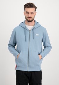 Felpa con zip azzurra chiara realizzata in tessuto morbido, con logo frontale, cappuccio con cordini e tasche a marsupio. Polsini e orlo a coste.