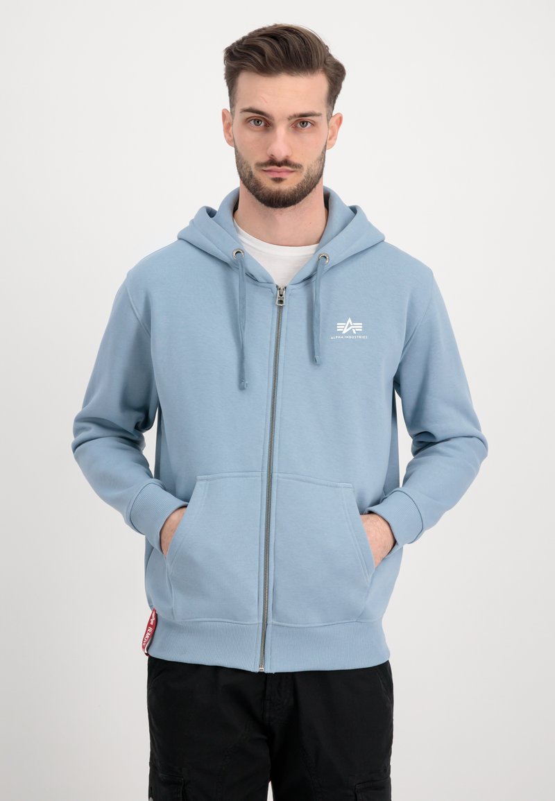 Svetlomodrá mikina na zips vyrobená z mäkkej tkaniny, s predným logom, kapucňou so sťahovacími šnúrkami a kengurími vreckami. Rúbkované manžety a lem.
