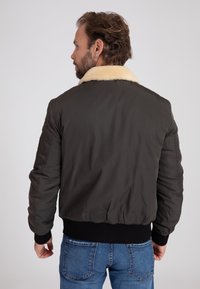 Ciemnozielona kurtka bombka z kołnierzem z kremowego, sztucznego barana, ściągaczami przy mankietach i u dołu; charakteryzuje się gładką fakturą i dopasowanym krojem.