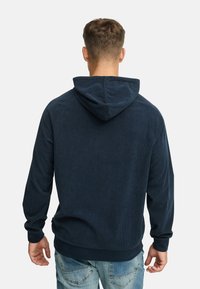 Mørkeblå corduroy hoodie med ribbet tekstur, snøre-hætte og lange ærmer. Har en solid kant og afslappet pasform.