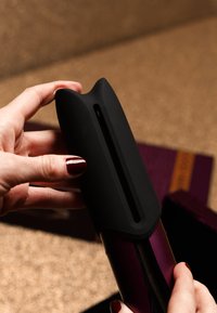 Schwarzer Silikongriff an einem lila-metallischen Gerät mit einem schmalen Schlitz. Der Griff hat eine glatte Textur und ist für eine ergonomische Handhabung konzipiert.