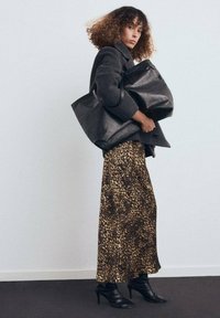 Bolso tote de cuero negro, abrigo de lana gris, falda larga de estampado de leopardo y botines negros de tacón, contra un fondo blanco liso.