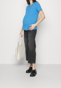 Niebieska koszulka z krótkim rękawem, czarne skrócone dżinsy, czarne buty na platformie oraz biała torba typu tote, noszone przez osobę z widoczną ciążą.