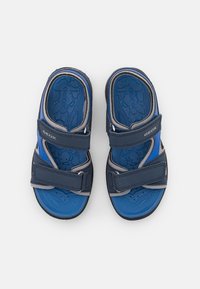 Blå och grå sandaler med gummisula, två justerbara Velcro-remmar och en texturerad fotbädd med cirkulära mönster.