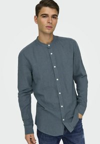 Camisa de color azul oscuro, de botón con cuello mao, mangas largas y un tejido texturizado. Presenta botones blancos visibles y un corte relajado.
