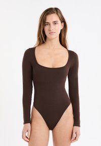 Brauner Body mit langen Ärmeln, mit Rundhalsausschnitt und hoch geschnittenen Beinen. Hergestellt aus einem glatten, enganliegenden Stoff mit nahtlosem Design.