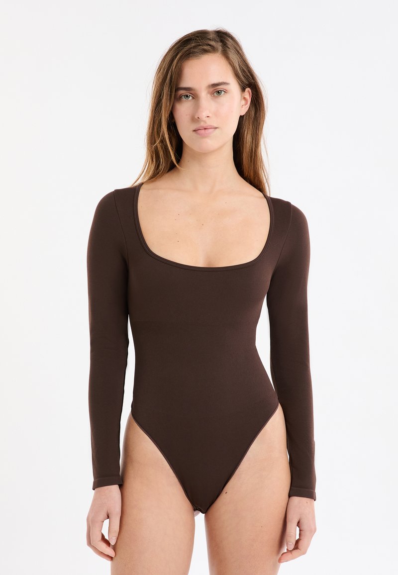 Brauner Body mit langen Ärmeln, mit Rundhalsausschnitt und hoch geschnittenen Beinen. Hergestellt aus einem glatten, enganliegenden Stoff mit nahtlosem Design.