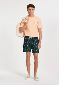 Light peach t-shirt with blue graphic, dark green shorts with pink starfish pattern, beige sneakers, and canvas tote bag.