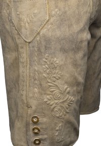 Světle hnědé lederhosen s jemnou květinovou výšivkou a postranní kapsou. Obsahuje čtyři dřevěné knoflíky a strukturovaný povrch.