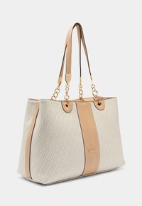 Sac cabas beige avec tissu à motifs, accents en cuir marron clair contrastants, ferrures dorées et doubles bandoulières.