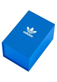 Plavi kartonski kutija s glatkom teksturom, s bijelim Adidas logotipom i dizajnom s tri pruge na vrhu. Zatvorena, pravokutnog oblika.