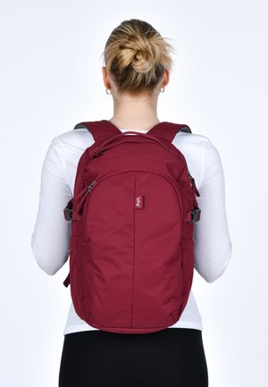 Zaino marrone con spallacci imbottiti, numerosi zips, tasca frontale e tasche laterali in rete. Tessuto testurizzato con chiusure regolabili.