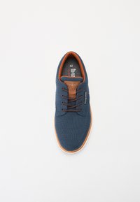 Zapatilla de lona azul con detalles en cuero marrón, punta redonda y cordones marrones. Talla marcada como 42 en la plantilla. Suela de goma plana y texturizada.