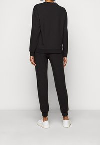 Svart bomullströja och matchande joggers, med ribbad mudd och midja, bärs med vita sneakers. Enkel design, enfärgad.