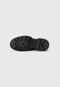 Semelle extérieure en caoutchouc noir avec des crampons profonds et un design à motifs pour une bonne traction. Surface lisse avec des accents surélevés et des rainures pour une meilleure adhérence.