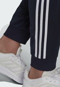 Marineblaue Sporthosen mit weißem Dreistrichdesign an den Seiten, ausgestattet mit einem schmalen Bund und kombiniert mit weißen Sportschuhen.