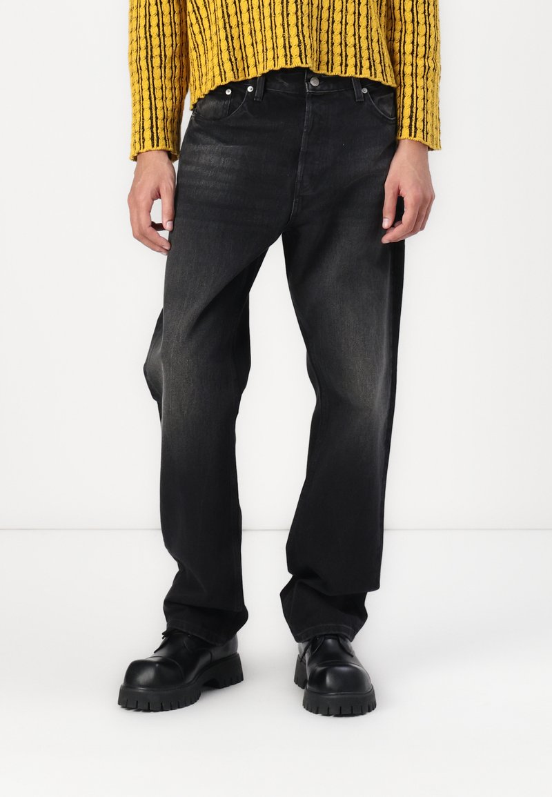 Sorte denim jeans med en afslappet pasform, der har fem lomme-design og diskret falmning. Parret med en tekstureret gul striktrøje.