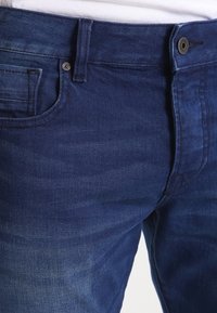 Vaqueros de mezclilla azul oscuro con un ligero desvanecimiento, que presentan bolsillos estándar, un cierre de botón metálico y detalles de costura sutiles.
