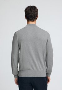 Pull en maille grise avec un col rond, des poignets et un ourlet côtelés, et une texture douce, montré de dos, mettant en valeur le tissu lisse.