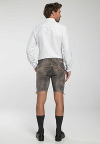 Traditionele herenbermuda's van verweerd bruin stof met decoratieve stiksels. Gecombineerd met een witte blouse met lange mouwen, grijze sokken en zwarte schoenen.