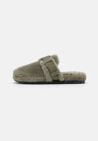 Gröna, fluffiga tofflor i päls med en bred rem, som har en logotyp och en texturerad svart sula. Avslappnad och lätt design för komfort.
