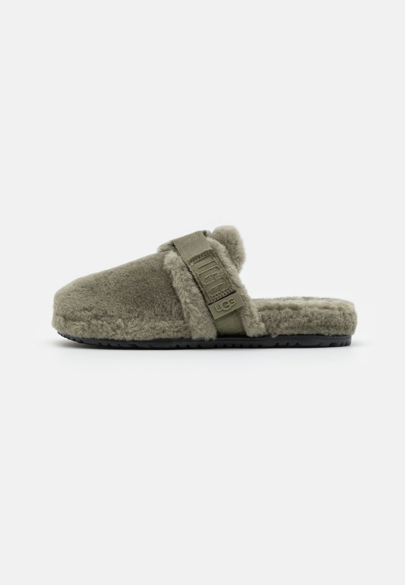Green, fluffy fur slippers with a wide strap, featuring a logo and a textured black sole. Casual and lightweight design for comfort.