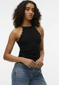 Top nero a collo alto con un tessuto a maglia testurizzato; presenta bordi ondulati e una vestibilità aderente, abbinato a jeans in denim azzurro chiaro.