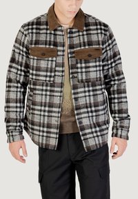 Camicia di flanella a quadri in nero, bianco e marrone, con colletto in velluto a coste e due tasche sul petto con chiusura a scatto.