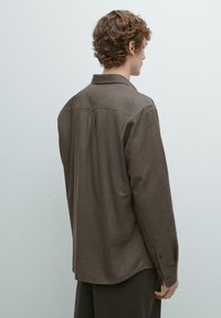 Braunes Langarmhemd mit Kragen, Rückenfalte und geknöpften Manschetten. Weiche Textur; lockere Passform mit abgerundetem Saum und minimalistischem Design.