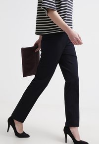 Pantaloni neri su misura con vestibilità dritta, abbinati a una maglietta a righe e tenendo in mano una clutch bordeaux, indossati con tacchi alti neri.