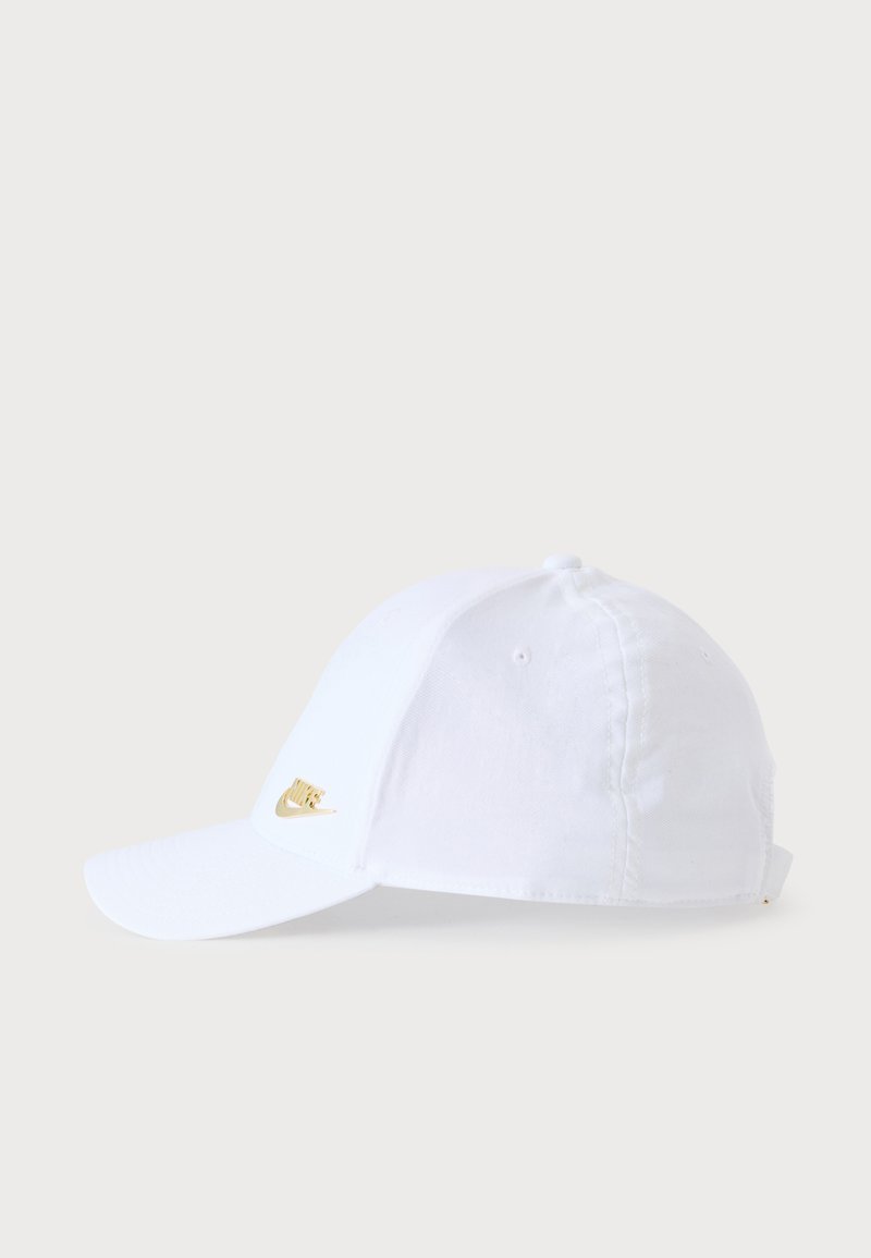 Casquette de baseball blanche Nike avec un logo swoosh doré sur l'avant, présentée sur un fond clair uni.