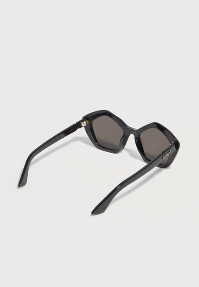 Black oversized hexagonal sunglasses with dark lenses and slightly curved temples on a light background.