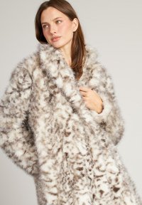 Płaszcz z futra sztucznego w beżowo-brązowy wzór w cętki, z szerokim kołnierzem i miękką, teksturowaną tkaniną, tworzący efektowną, obszerną sylwetkę.