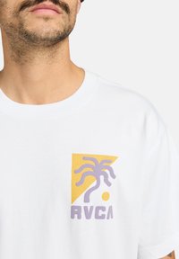 Biely bavlnený tričko s grafickým dizajnom, ktorý zobrazuje žltý trojuholník a motív fialovej palmy, pod ktorým je uvedený názov značky "RVCA".