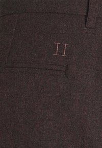 Pantalones de lana en un color burdeos oscuro con una superficie texturizada, que cuentan con un bolsillo trasero y un detalle bordado en color rosa claro con "II".