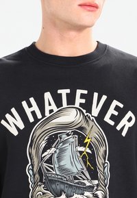 Felpa nera in cotone con grande testo bianco "WHATEVER" e un grafico di una nave, onde e un fulmine al centro.