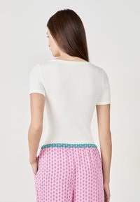 Maglietta bianca a maniche corte con righe, abbinata a pantaloni rosa con motivo e vita turchese. Il design sottolinea il contrasto di texture e colori.