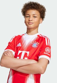 Rød Bayern München-drakt med hvite detaljer, med et gradientmønster, logo på venstre bryst og sponsorskilt på ermene.