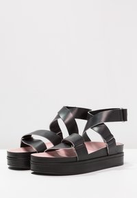 Černé kožené platformové sandály s kříženými pásky, hladkým povrchem a růžovou stélkou s blokovým podpatkem.
