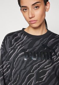 Felpa nera con un motivo a strisce zebra grigio e nero, dotata di un logo "PUMA" lucido in nero sul petto e di un piccolo emblema di un gatto nero.