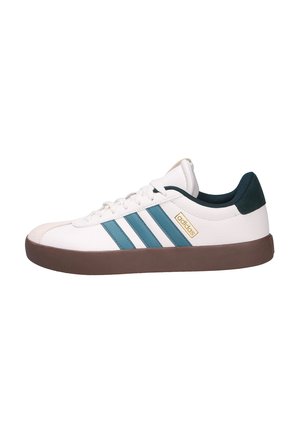 Zapatillas blancas con rayas en azul verdoso, suela de goma marrón y parte superior texturizada. Presenta un logo dorado y un acento en verde oscuro en el talón.