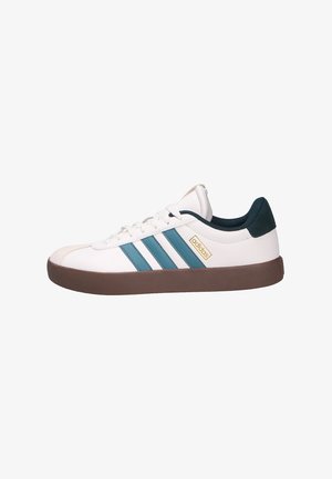 Zapatillas blancas con rayas en azul verdoso, suela de goma marrón y parte superior texturizada. Presenta un logo dorado y un acento en verde oscuro en el talón.