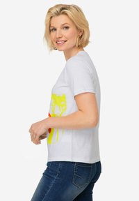 Weißes Baumwoll-T-Shirt mit einem mehrfarbigen Grafikdruck in Gelb und Rot, runder Ausschnitt und kurzen Ärmeln, kombiniert mit dunklen Jeans.